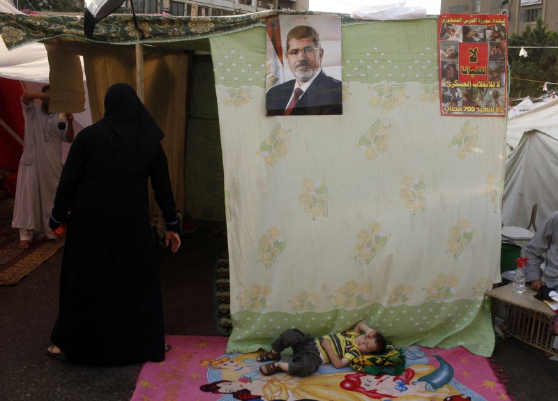 Criança descansa deitada debaixo de um cartaz do presidente deposto Mohamed Mursi | Asmaa Waguih/Reuters
