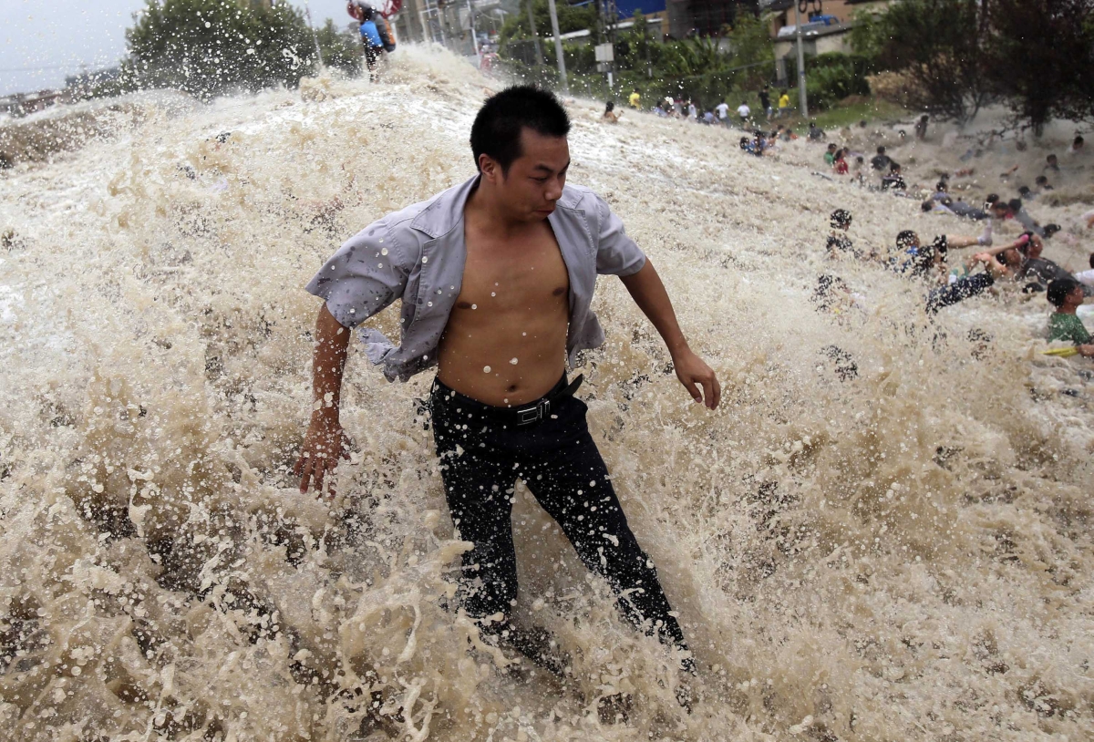 Homem luta contra as ondas ocasionadas pela subida no nível do rio Qiantang | Reuters/China Daily