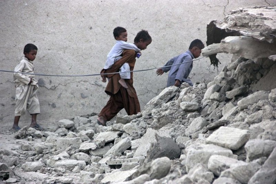 Crianças sobreviventes do terremoto de 7,7 graus na escala Ritcher caminham em meio a destruição do distrito de Awaran | REUTERS/Sallah Jan