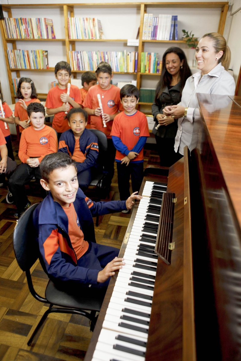Murilo, 9 anos, visto pela diretora Cibele (ao lado do piano) e a professora Anne: a escola tem piano, mas ainda não há aulas por falta de verbas | André Rodrigues/ Gazeta do Povo