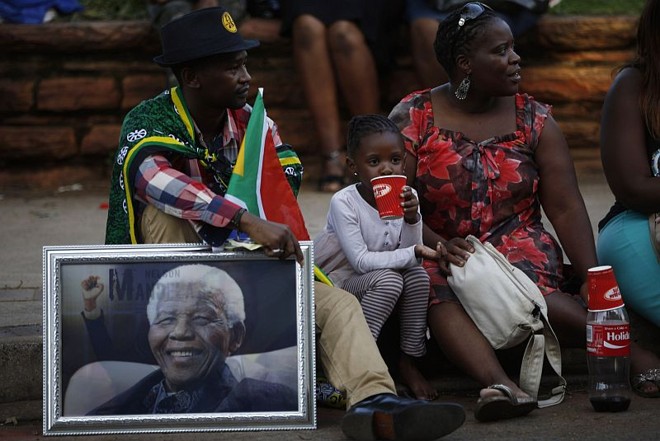 Casal segura retrato de Nelson Mandela próximo ao local onde o corpo do líder sul-africano é velado em Pretória | REUTERS/Mike Hutchings
