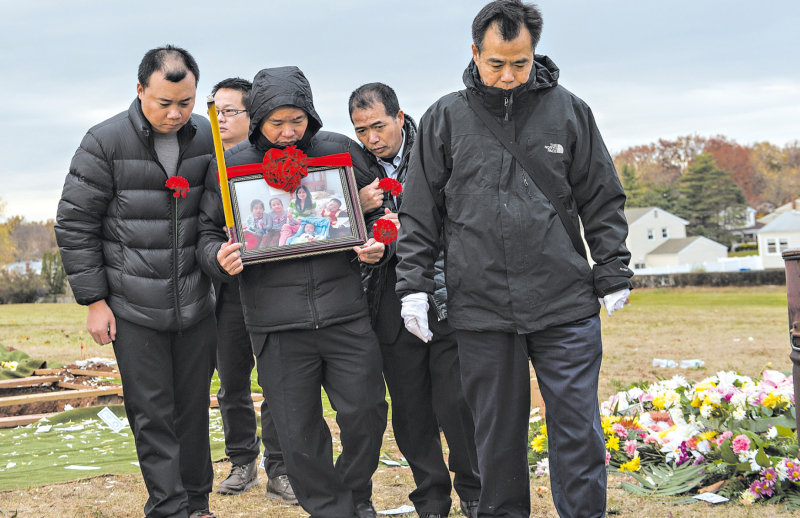 Yilin Zhuo segura fotografia de sua família no enterro da esposa e dos quatro filhos, que foram mortos a facadas em outubro, no Brooklyn | Robert Stolarik/The New York Times