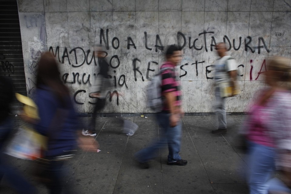 Pedestres passam por muro pichado com a fase: Não à ditadura de Maduro, no distrito de Chacao, em Caracas | Tomas Bravo/Reuters