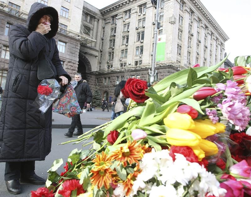 Mulher deposita flores em homenagem aos ucranianos que morreram durante os protestos | EFE/Igor Kovalenko