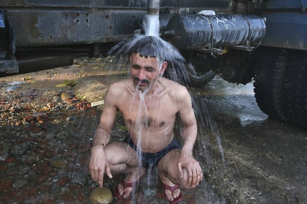 Um homem toma banho sentado sob um tanque de água em Jammu | REUTERS/Mukesh Gupta