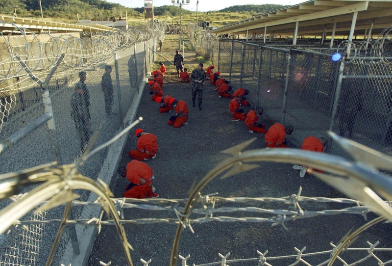 Detentos em macacões alaranjados em área vigiada pela polícia no Camp X-Ray, na base naval de Guantánamo, em Cuba | Shane T. McCoy/Reuters