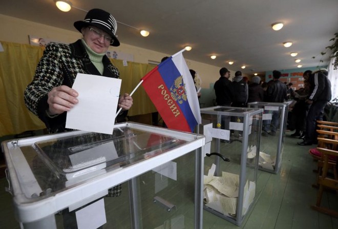 Mulher segura bandeira da Rússia ao depositar voto na urna no referendo sobre a anexação da Crimeia | REUTERS/Sergei Karpukhin