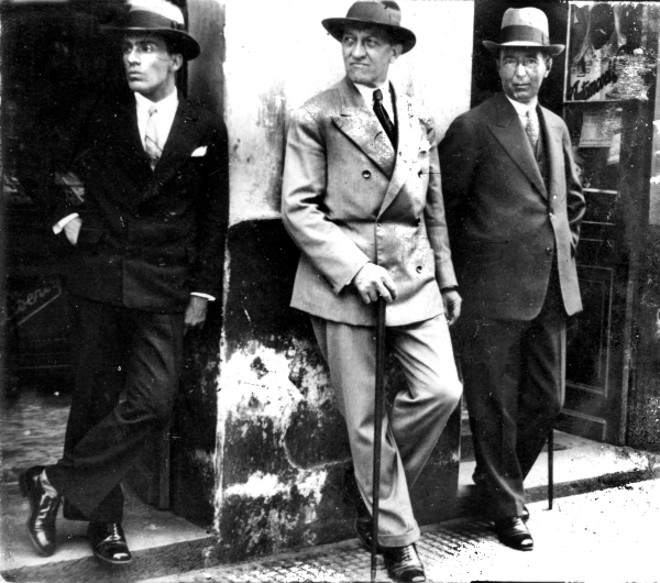 O escultor João Turin, entre dois amigos, na porta do Café Belas Artes, apreciando o movimento no Senadinho, no final da década de 1930 | 