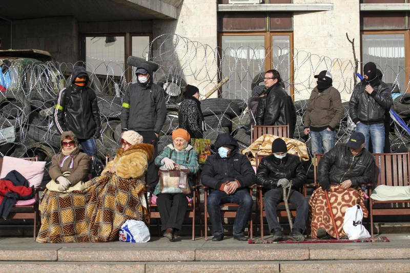 Manifestantes pró-Rússia ao lado de senhoras com seus cobertores perto de uma barricada diante de um prédio público em Donetsk | Reuters