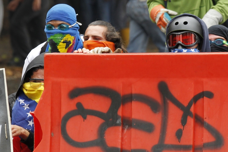 Estudantes tentam se proteger atrás de barricada enquanto participam de manifestação contra o governo do presidente Nicolás Maduro, nas ruas caraquenhas | Christian Veron/Reuters