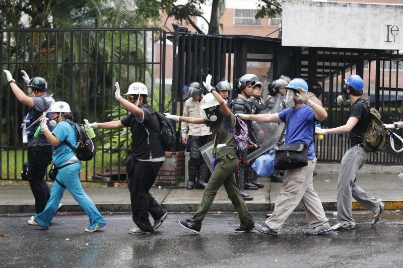 Manifestantes trabalhando como paramédicos andam com as mãos para cima em meio a policiais, em Caracas | Jorge Silva/Reuters