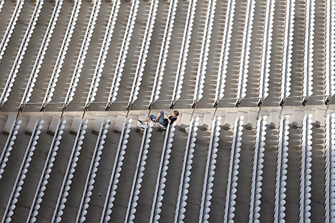 Funcionária do estádio aproveita o sol que bate na arquibancada sul para descansar. | 