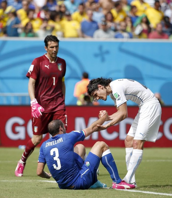 O uruguaio Edinson Cavani (dir.) ajuda o jogador da seleção italiana Giorgio Chiellini (centro) a se levantar | 