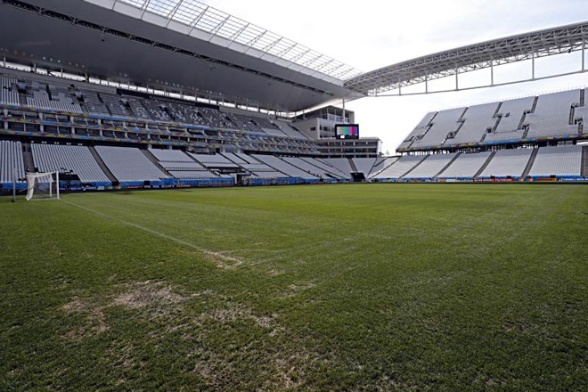 A beira do gramado cheia de areia e o telão de alta definição permanentemente ligado, ao fundo. | 