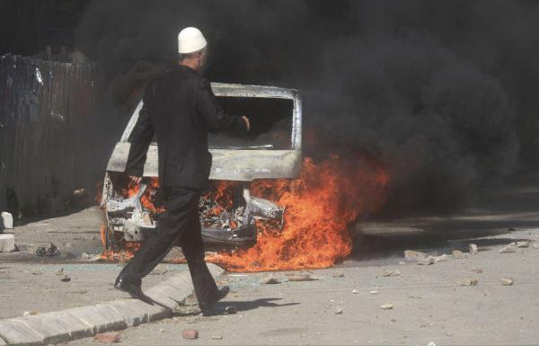 Um homem passa por um carro em chamas incendiado por albaneses durante um protesto em Mitrovica no domingo (22). A polícia de Kosovo disparou gás lacrimogênio e balas de borracha contra os manifestantes | REUTERS/Hazir Reka