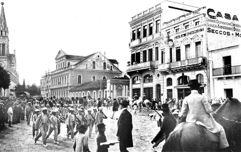 Alunos da Escola de Artífices de Curitiba desfilam pela Praça Tiradentes, em 21 de abril de 1913. Note-se a preocupação de mostrar a formação militar, cada criança leva ao ombro uma carabina de madeira | Acervo Cid Destefani