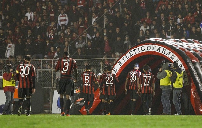 Volta à Vila -O regulamento da Série A do Brasileirão exige 15 mil lugares, inviabilizando o Janguito, mesmo com as arquibancadas tubulares. Além disso, o MP proibiu que houvesse Atletibas no campo do Jotinha, pois há poucos acessos. Assim, o Atlético teve de ir, na reta final do Paranaense de 2013, fazer um acordo com o Paraná para usar a Vila Capanema e, na falta desta, a Vila Olímpica. Com isso, o Atlético mandou o Atletiba decisivo do 2.º Turno do Paranaense e uma das partidas da decisão no Boqueirão, pois a Vila Capanema teve um acidente de manutenção que fez com que tivesse de trocar todo o gramado. Antes de voltar ao Durival Britto, ainda mandou uma partida contra o Cruzeiro lá, arrancando reclamações dos mineiros. O acordo fez o Furacão se responsabilizar com toda a manutenção e gastos dos dias de jogos, assim como a reconstrução do alambrado que caiu no Atletiba. Além disso, o clube lançou mão até de um túnel inflável para a entrada em campo. A Vila Capanema foi fundamental para a boa campanha no Brasileirão, mas a estadia no Brasileirão foi interrompida por uma punição por uma briga entre a própria torcida no Atletiba em que o alambrado caiu. | 