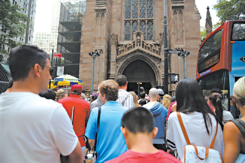 Turistas aguardando diante da Trinity Church, que oferece banheiros públicos com pés-direitos altos e vitrais | nicole bengiveno/The New York Times