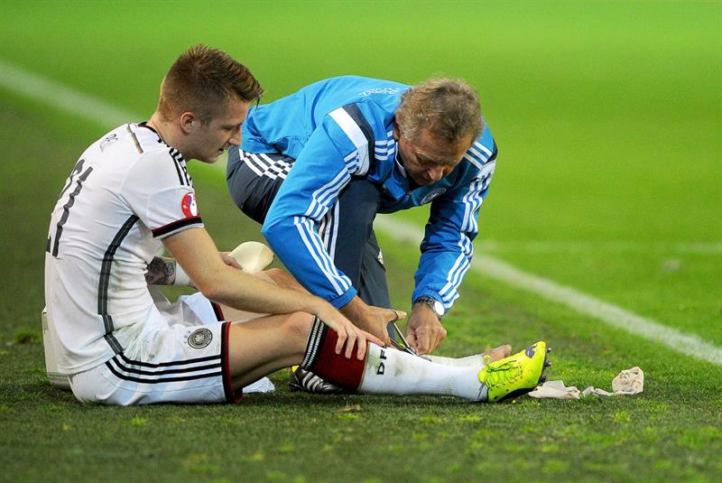 O alemão Marco Reus (à esquerda) recebe atendimento médico durante jogo da Alemanha contra a Escócia, nas Eliminatórias da Eurocopa de 2016 | EFE/EPA/JONAS GUETTLER