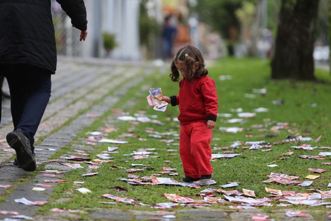 Menina brinca com santinhos em frente ao Colégio Estadual Professor Cleto, no Centro de Curitiba | 