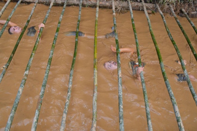 Os competidores tiveram de atravessar um tanque de lama coberto por uma grade de bambu. | 