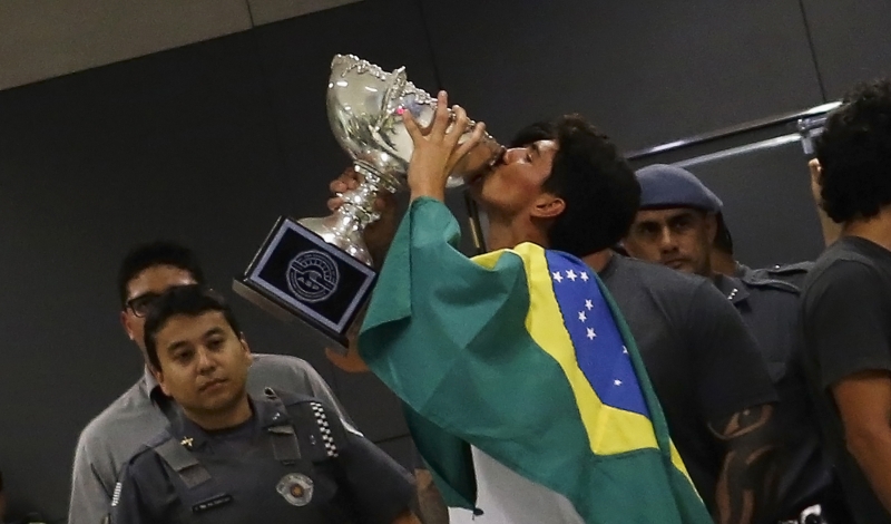 Enrolado com a bandeira do Brasil, Gabriel Medina beija o troféu da conquista mundial na chegada em Guarulhos: recepcionado com os gritos de é campeão | Nacho Doce/Reuters