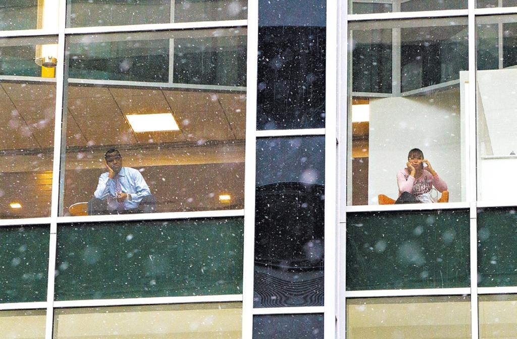 As pessoas olham pela janela do escritório e veem a neve cair no centro da Filadélfia, na Pensilvânia | Michael R. Sisak/Associated Press