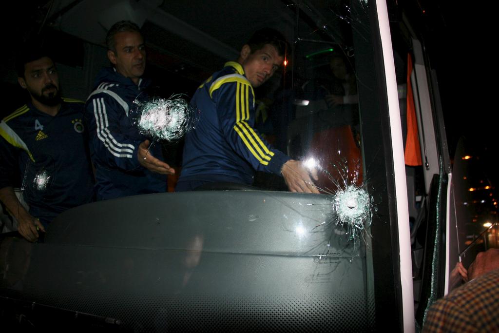 O técnico Kartal e os jogadores Emre e Bekir conferem os buracos de balas no para-brisa do ônibus da equipe. | Stringer/Reuters
