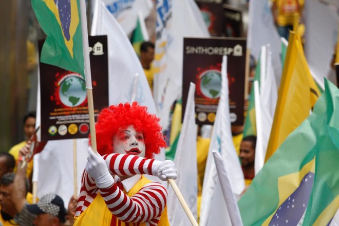 No saguão do Museu de Arte de São Paulo (MASP), cerca de 700 pessoas se reuniram com cartazes, muitas fantasiadas como o palhaço “Ronald McDonald”, e no final incendiaram um caixão simbolizando o enterro do personagem. | Carlos Villalba R./EFE