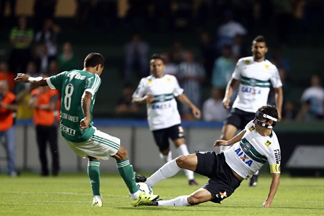 O palmeirense Cleiton Xavier disputa a bola com o “mascarado” coxa-branca Lúcio Flávio, logo no início do duelo no Couto Pereira. | Albari Rosa/Gazeta do Povo