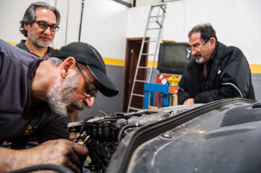 Elia Amma (em pé, à esquerda) ensina o trabalho na oficina mecânica para um refugiado sírio recém-chegado ao Brasil. | Thyago Souza / Arquivo pessoal.