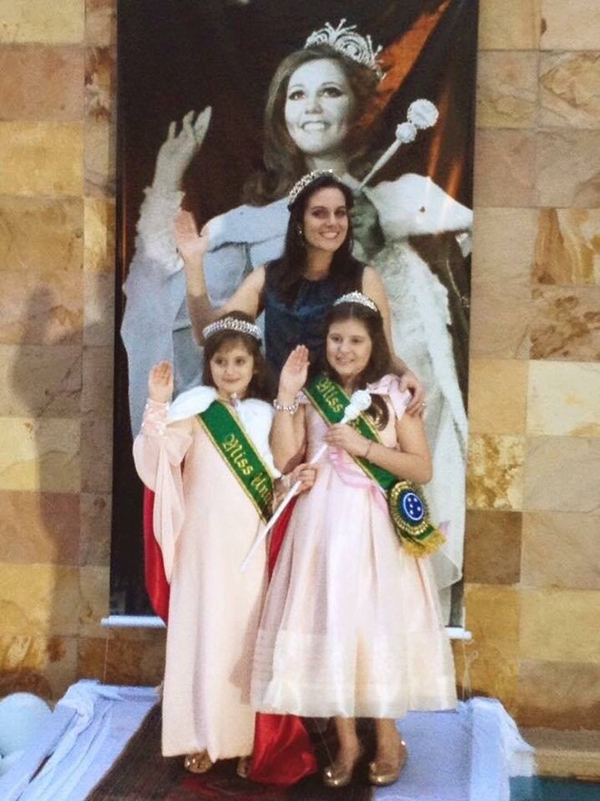 A filha Juliana Genta e as netas Giogia e Laura em frente ao pôster de Wilza nos tempos de miss. | Arquivo da família