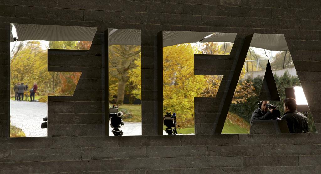 Logo da Fifa mostra jornalistas refletidos na entrada da sede, em Zurique, durante reunião extraordinária da instituição. | Arnd Wiegmann/Reuters