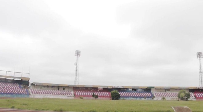 Árvores crescem no gramado, em frente à arquibancada. | 