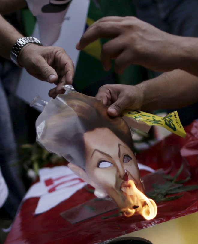Manifestantes, em Brasília, ateiam fogo a uma máscara de papel com a foto da presidente Dilma Rousseff. | Ueslei Maarcelino /Reuters