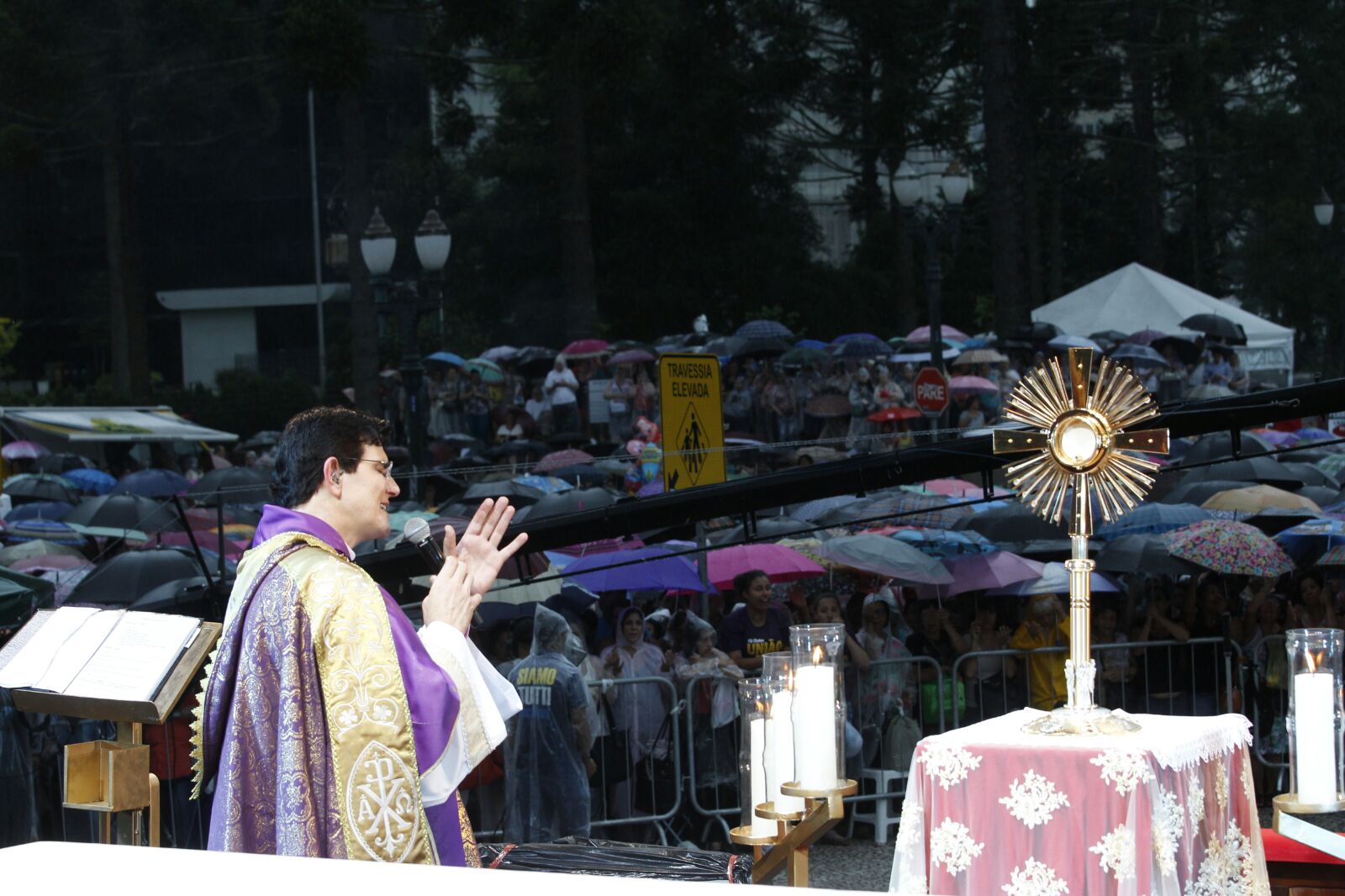 Padre Reginal Manzotti na missa, com a multidão ao fundo, usando guarda-chuvas. | Fotos: Daniel Castellano/Gazeta do Povo