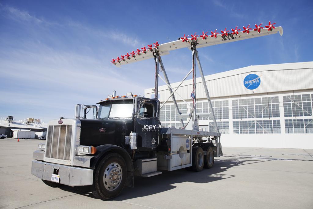 Caminhão leva um  protótipo do sistema pensado pela Nasa: uma asa de pouco mais de 9 metros, a mesma de um pequeno avião, equipada com 18 motores elétricos, cada um com uma pequena hélice vermelha. | EMILY BERL/NYT
