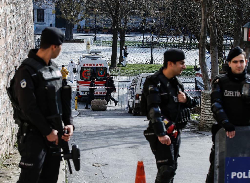 Policiais são vistos na entrada da Mesquita Azul, em Istambul. Ao fundo, médicos legistas trabalham no local da explosão | BULENT KILIC/AFP