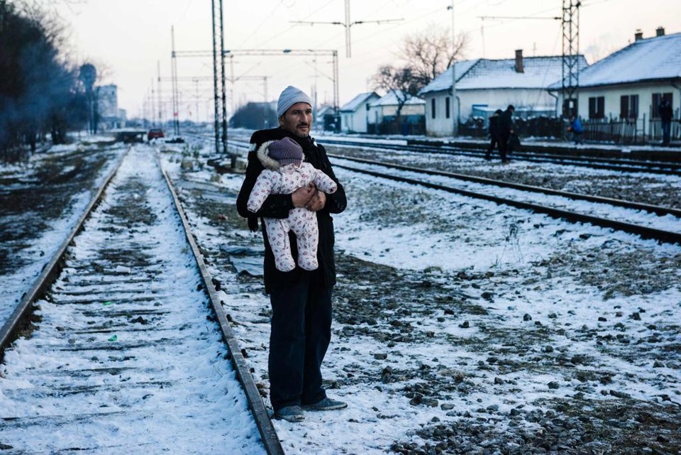 Sírio segura uma criança enquanto espera um trem em Preservo, cidade da Sérvia | DIMITAR DILKOFF/AFP