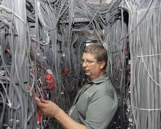 Um dos técnicos de um data center é fotografado em meio a um emaranhado de fios. | Peter Garritano/petergarritano.com