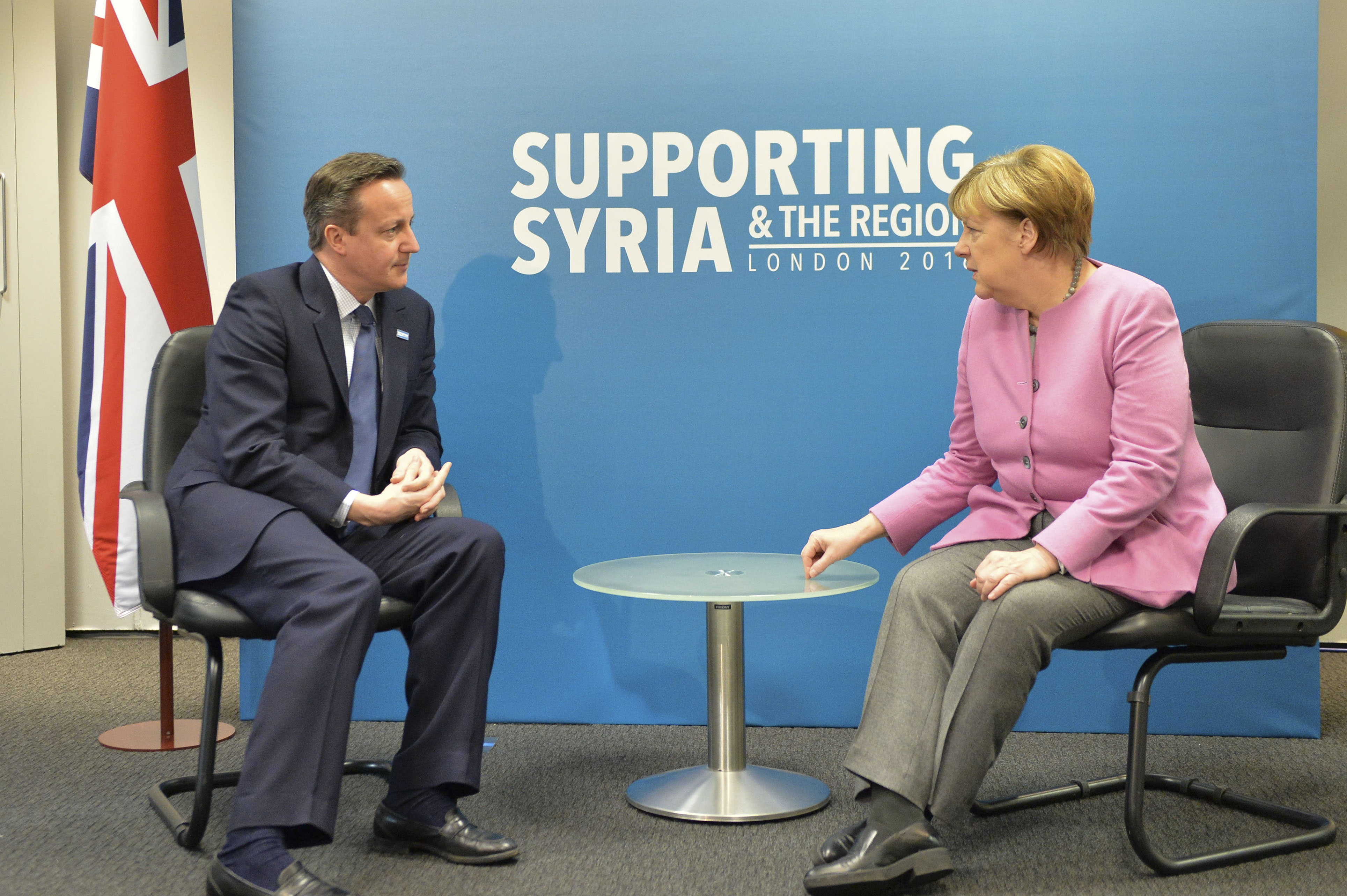 A chanceler alemã Angela Merkel (dir.) tem se mostrado bastante receptiva aos migrantes . Na foto ela conversa com o primeiro ministro britânico, David Cameron, na abertura da sessão que discutiu a situação síria, no começo de fevereiro. | Georgina Coupe/ The Prume Minister´s Office/Fotos Públicas