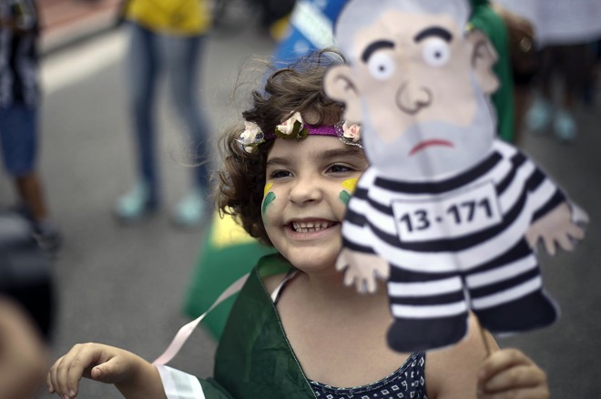Em São Paulo, criança participa da manifestação na Avenida Paulista, segurando caricatura do ex-presidente Lula em roupas que remetem às de presidiários | Miguel Schincariol/AFP