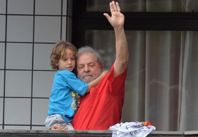 Da sacada de seu apartamento em São Bernardo do Campo e segurando o neto Pedro, o ex-presidente Lula acena para simpatizantes | NELSON ALMEIDA/AFP