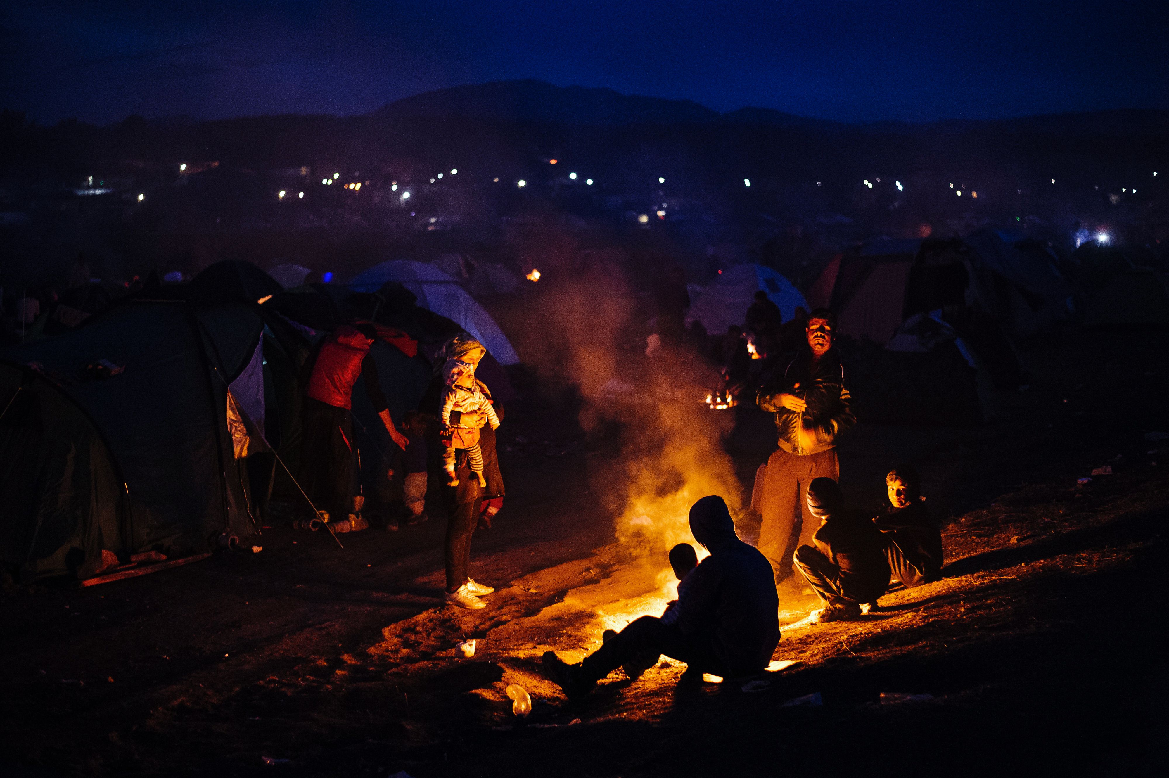 Família se aquece em fogueira no acampamento improvisado na fronteira da Grécia e Macedônia | DIMITAR DILKOFF/AFP