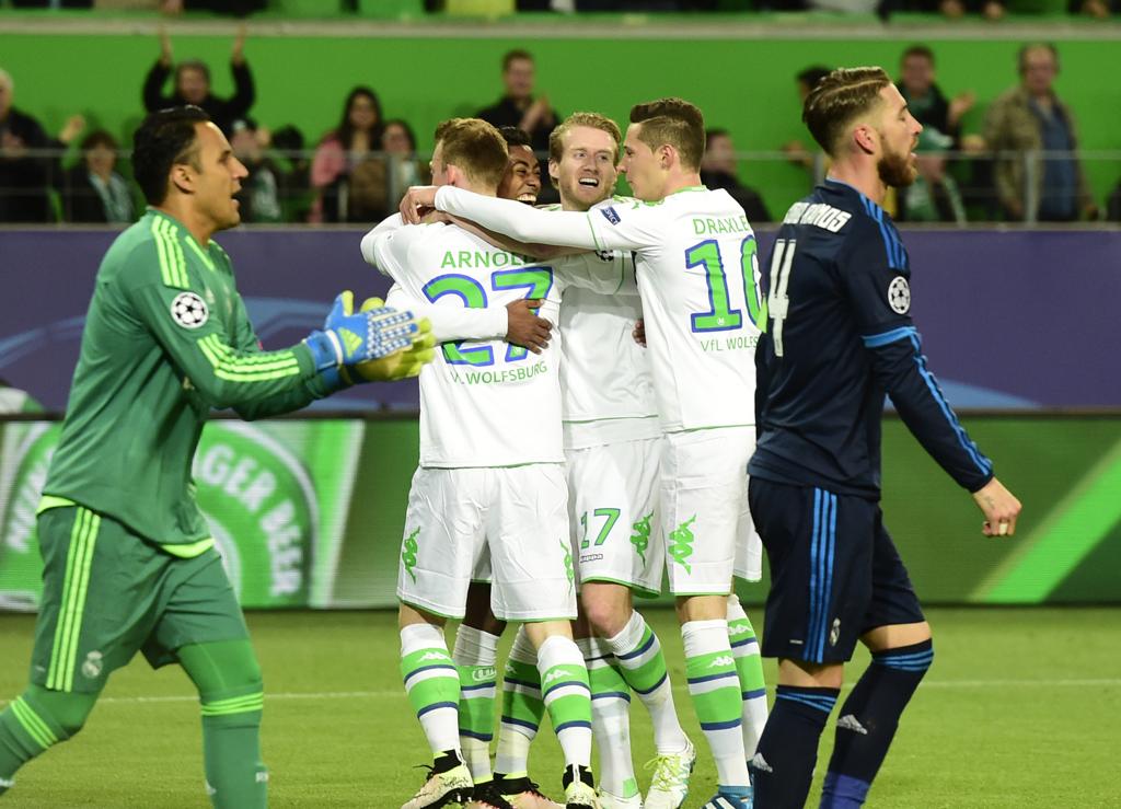 Jogadores do Wolfsburg comemoram o primeiro gol, de pênalti. Real precisa vencer agora em casa por três ou mais gols de diferença para se classificar. | JOHN MACDOUGALL/AFP