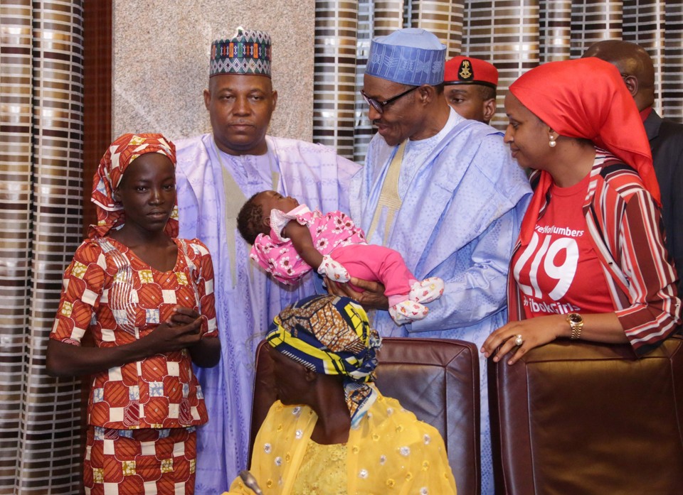 O presidente nigeriano Mohammadu Buhari segura o bebê de Amina Ali (de laranja), que escapou do Boko Haram dois anos depois de ser sequestrada | STRINGER/AFP