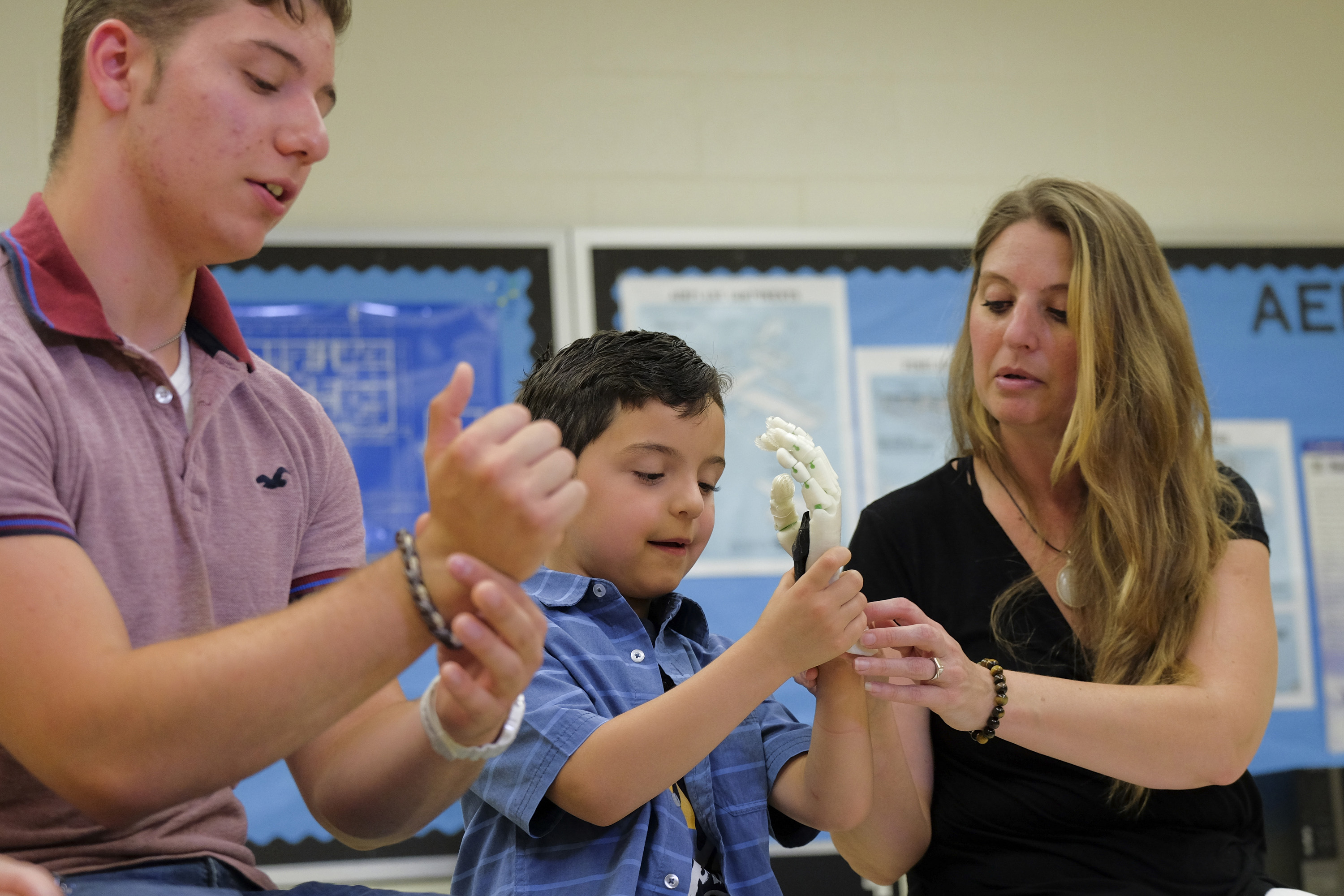 Gabriel Filippini, 16, mostra ao irmão, Lucas, de 6 anos, como a prótese da mão funciona. Ao lado, a mãe Romina Barrera ajuda o filho a colocar o aparato | Jahi Chikwendiu/The Washington Post