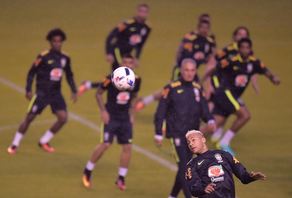 Neymar afasta a bola de cabeça em treino para o duelo com o Equador. Ao fundo, Tite observa a atividade em meio à defesa da seleção. | Rodrigo Buendia/AFP