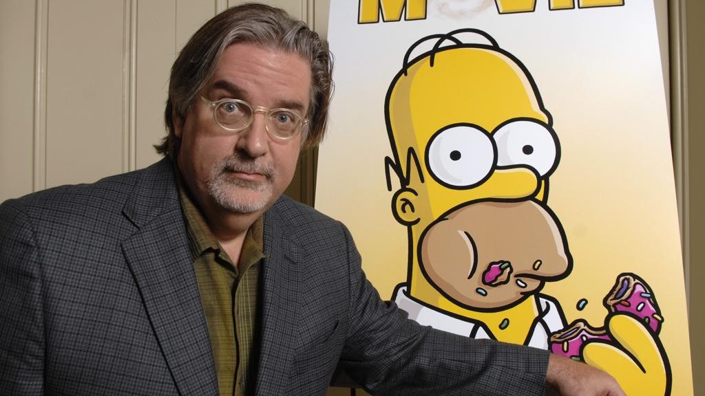 Matt Groening, criador dos Simpsons, ao lado de cartaz com seu principal personagem: Homer Simpson