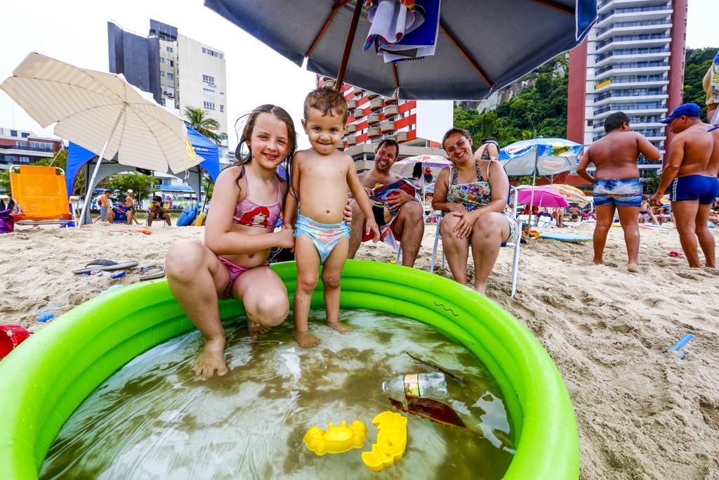 Fábio e Kamylla Moura assistem aos filhos se refrescando na piscininha montada na areia | Lineu Filho/Tribuna do Paraná